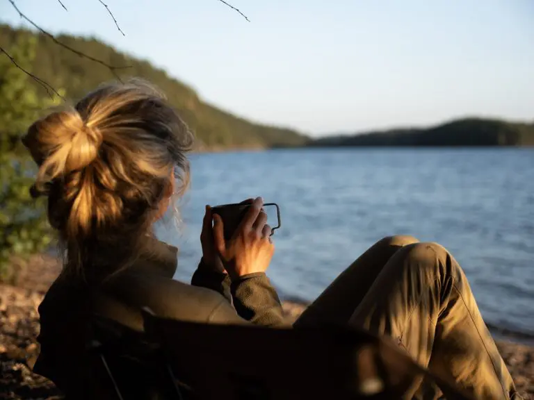 woman drinking coffee by lake at sunset