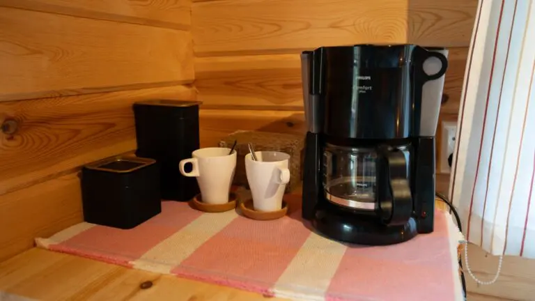 coffee machine and mugs on a striped mat in a wooden cabin