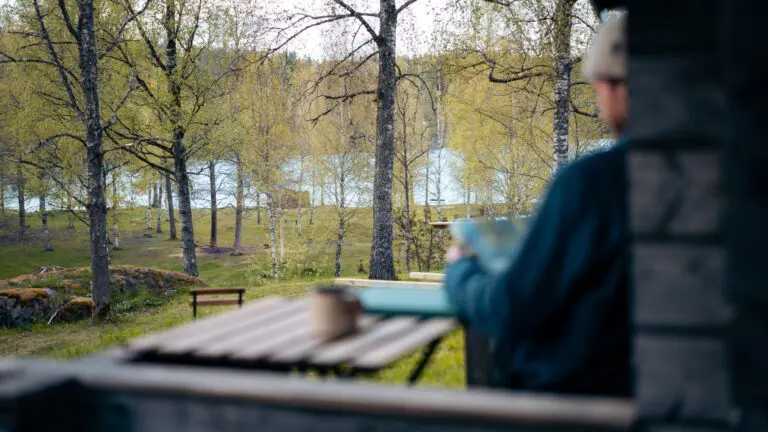 person reading by a lake in a forest hut
