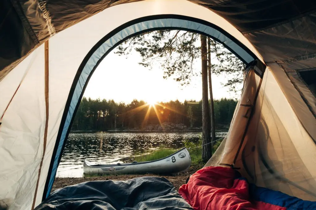 view from inside a tent of a lake, forest, and canoe at sunset