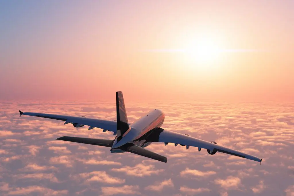 airplane flying above clouds at sunset