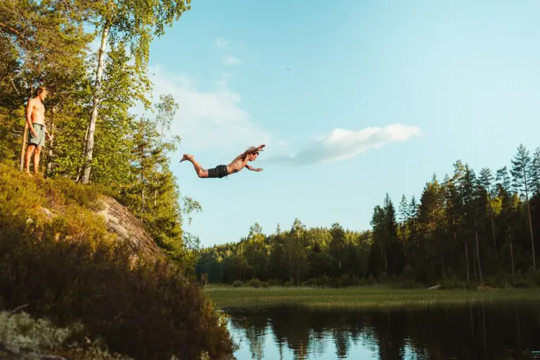 man cliff jumping into lake with friend watching