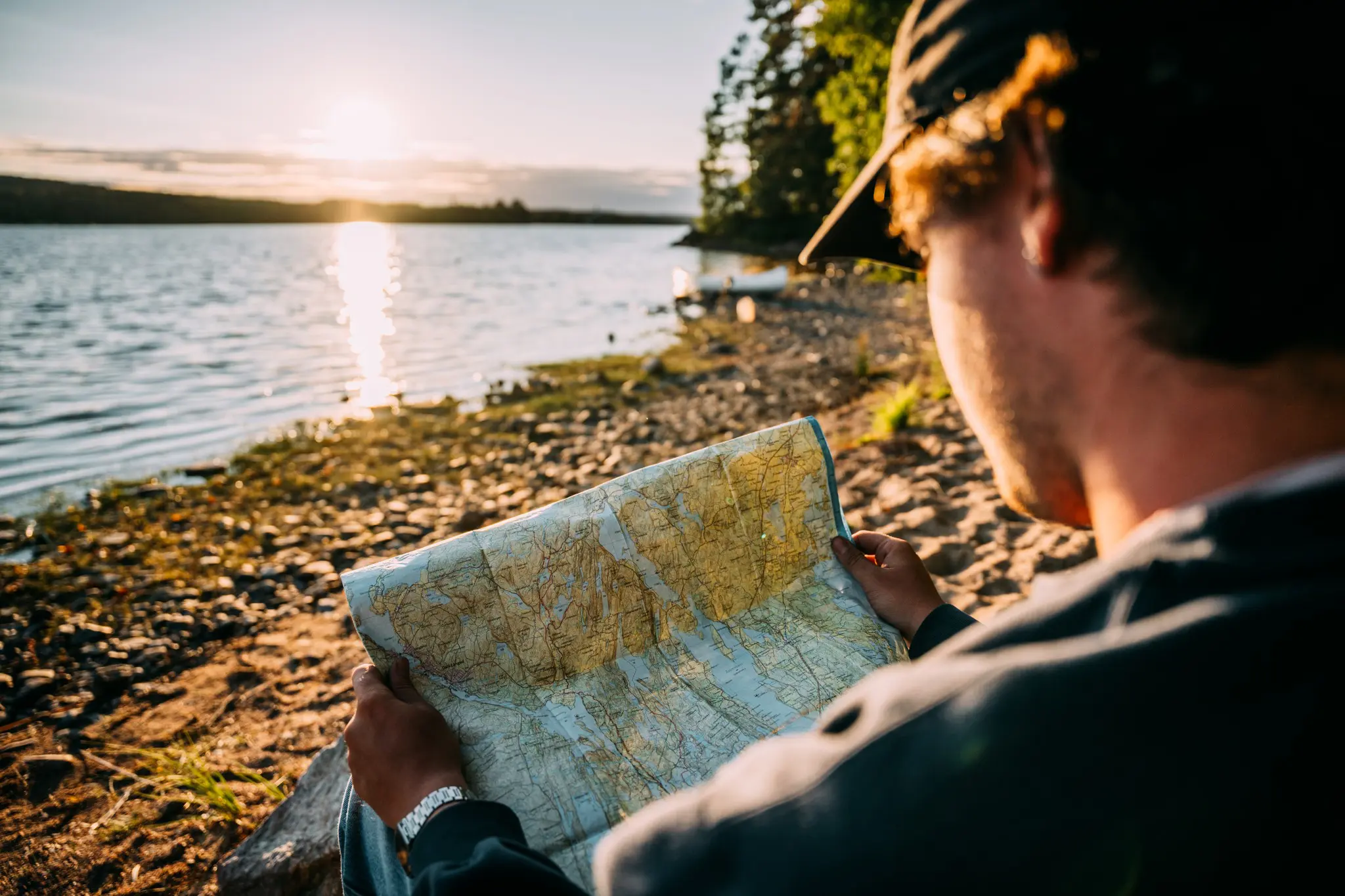 person in cap reading map by lake at sunset