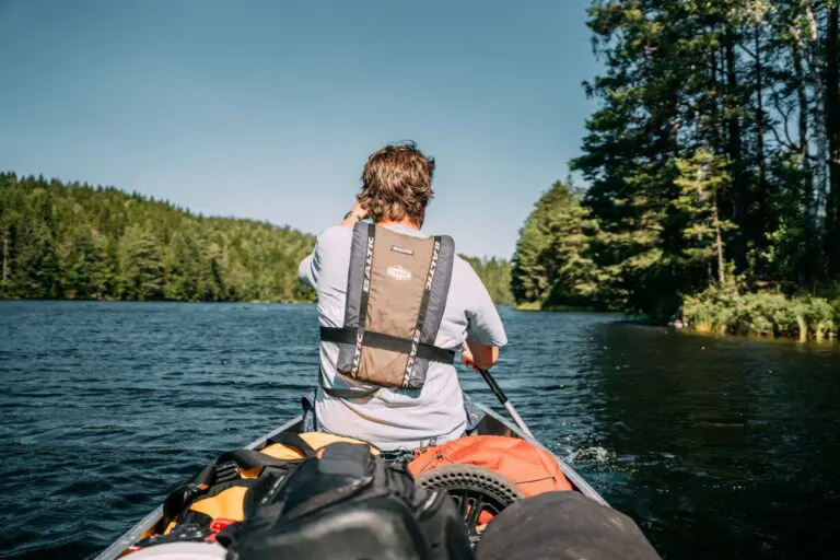 person paddling a canoe on a lake surrounded by forest