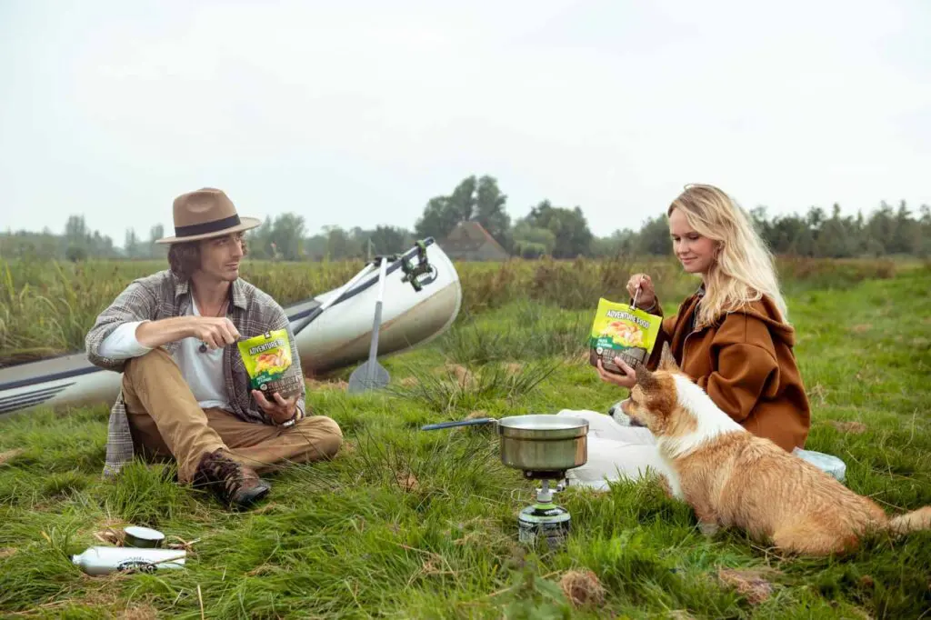 couple and dog camping with canoe eating adventure food