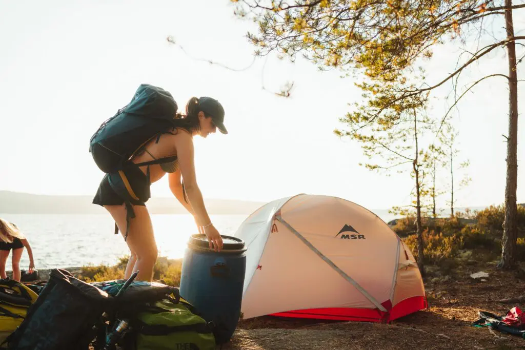 woman setting up camp by lake with tent and backpack