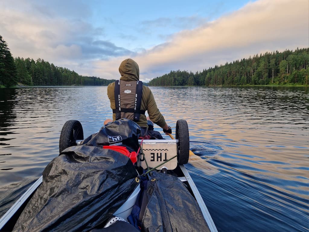 Een kano volgeladen met waterdichte drybags en een kanokarretje vaart over een rustig meer in Värmland Zweden tijdens een georganiseerde kanoreis.